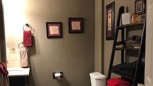 Une salle de bain équipée de toilettes, d’un lavabo et d’un porte-serviettes. Deux certificats encadrés sont accrochés au mur.