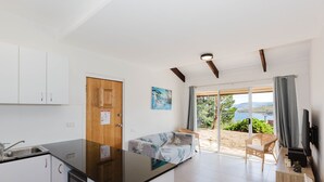 A modern kitchen with white cabinets, a wooden door, and a dining area with a sofa and wicker chairs. - Kooringa - 1/8 Townsend Street (Jindabyne)