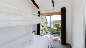 A bedroom with a bunk bed, a window with black curtains, and a view of a lake and hills. - Kooringa - 1/8 Townsend Street (Jindabyne)