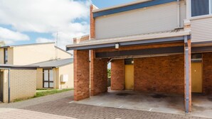 A building with a covered parking area, brick walls, and a garage door. - Kooringa - 1/8 Townsend Street (Jindabyne)