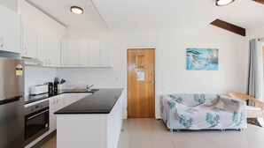 A modern kitchen with white cabinets, a black countertop, and stainless steel appliances. There's a wooden door with a notice on it, and a painting of a snowy landscape on the wall. - Kooringa - 1/8 Townsend Street (Jindabyne)