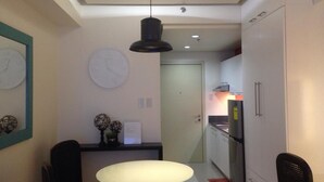 A compact kitchen with a round table, two chairs, a clock, and a refrigerator.