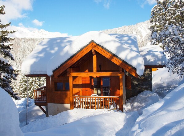 Une cabane en bois dotée d’un porche, entourée d’arbres et de montagnes couverts de neige.