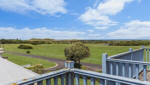 A view from a balcony overlooking a green field, a curved road, and a distant coastline. - Bella On Victoria - with ocean views (Port Fairy)