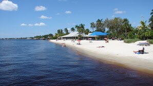 Una playa con orilla de arena blanca, un edificio de techo azul y palmeras.