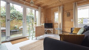 A wooden interior with a sofa, TV, and a dining area with chairs and a table. - Moyo Kijani Cosy Lodge (Zandvoort)