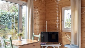 A wooden-paneled room with a TV on a white stand, a small table with a vase, and a chair. - Moyo Kijani Cosy Lodge (Zandvoort)
