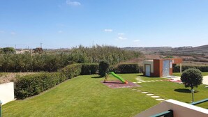 A well-maintained grassy area with a green slide, a small brick building, and a clear view of the surrounding landscape.
