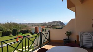 A balcony with a view of a hilly landscape and a distant mountain.