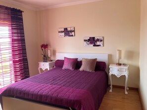 A bedroom with a large bed, two nightstands, a wall-mounted artwork, and a window with curtains.