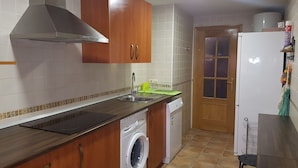 Een kleine keuken met houten kastjes, een roestvrijstalen spoelbak, een wasmachine en een koelkast.