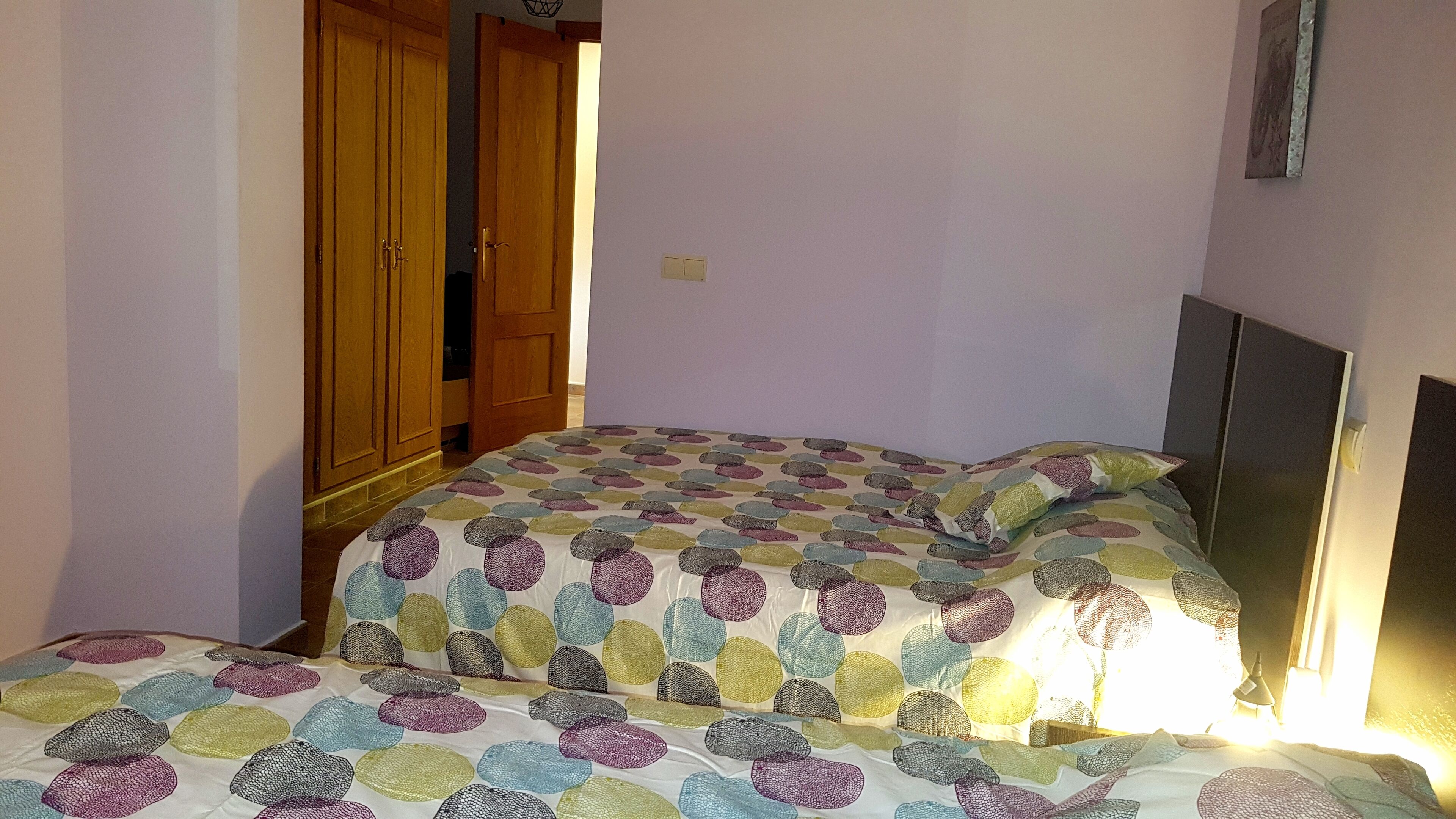 Une chambre à coucher avec un lit recouvert d’une couvre-lit à motifs, une armoire en bois et un luminaire fixé au mur.