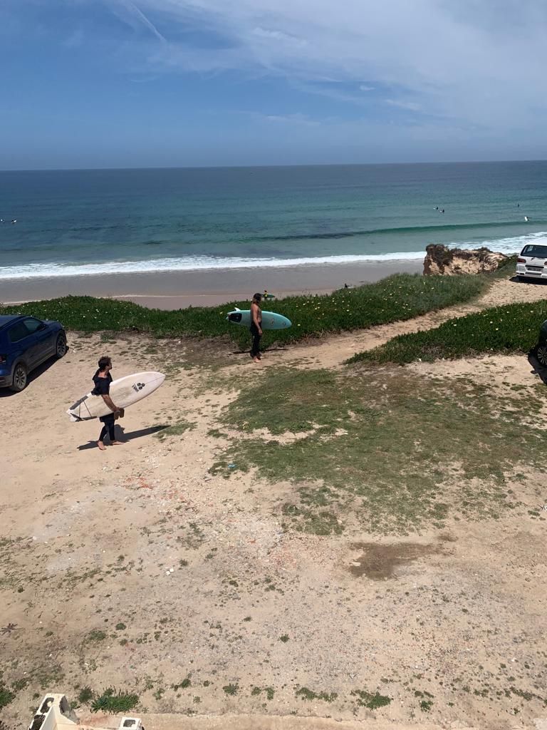Een strand met een auto, een surfplank en een persoon die loopt.