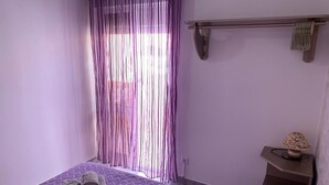 Ein Schlafzimmer mit Bett, Nachttisch, Lampe und einem Fenster mit Vorhängen.