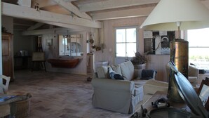 Een ruime woonkamer met een hoge plafond, een bank, een lamp en uitzicht op de keuken door een open deur.