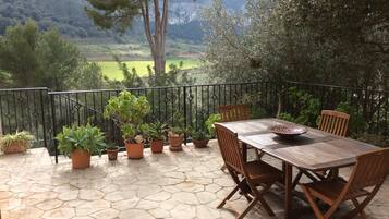 A patio with a table and chairs, surrounded by potted plants and a view of a mountainous landscape.