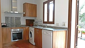 Una cocina compacta con armarios de madera, horno empotrado, lavadora y lavavajillas.