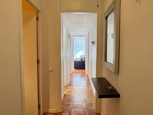 A hallway with a patterned wooden floor, a black shelf with keys, and a framed mirror on the wall.