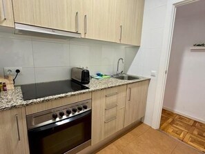 Uma cozinha compacta com fogão, forno, pia e armários de cor clara.