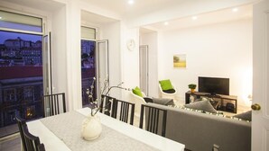 A modern living room with a dining area, a sofa, a TV, and a balcony with a city view. - Lisbon Amazing Castel View (Lisboa)