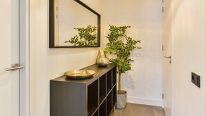 Un pasillo con un espejo, una consola, un cuenco, un jarrón y una planta en maceta.