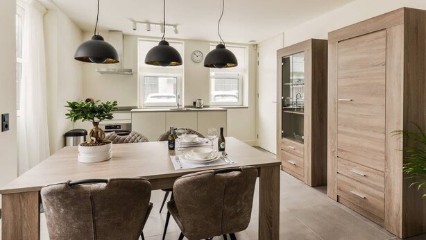 Una cocina moderna con una isla central, iluminación colgante y un armario de madera.