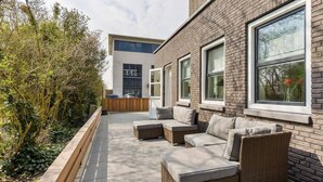 Un espacio al aire libre con mobiliario de mimbre y ventanas grandes.