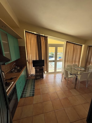 A compact kitchen with a dining area, a TV, and a view through the glass door.
