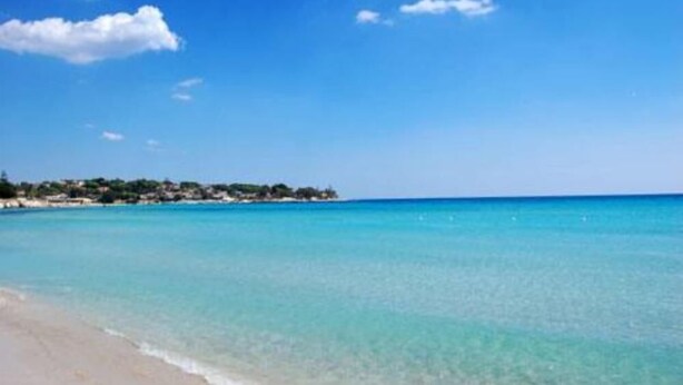 Une plage à l’eau turquoise et limpide, avec une côte lointaine parsemée de bâtiments.