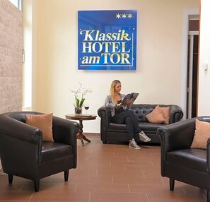 A hotel lobby with a large sign reading 'Klassik HOTEL am TOR,' two leather sofas, a small table with a vase and wine glass, and a brick wall. - Klassik Hotel Am Tor (Weiden in der Oberpfalz)