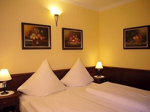 A hotel room with a bed, two bedside tables with lamps, and three framed fruit paintings on the wall.