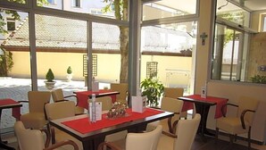 A restaurant with outdoor seating, tables with red placemats, and chairs with wooden armrests.
