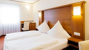 A hotel room with a double bed, a wooden headboard, a bedside table, and a desk with a chair.