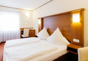 A hotel room with a double bed, a wooden headboard, a bedside table, and a desk with a chair. - Klassik Hotel Am Tor (Weiden in der Oberpfalz)