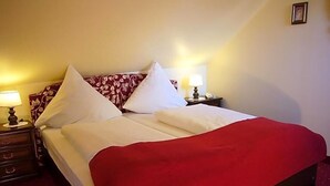 A double bed with a red blanket, two bedside tables with lamps, and a patterned headboard. - Klassik Hotel Am Tor (Weiden in der Oberpfalz)