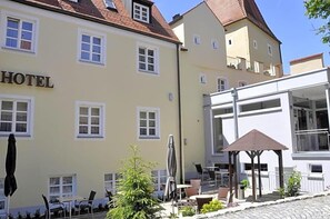 A hotel with a yellow facade, multiple windows, outdoor seating, and a covered patio area.