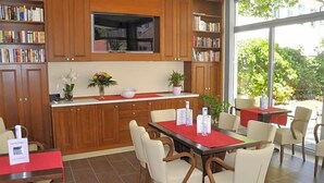 A modern kitchen with wooden cabinets, a dining area with white chairs, and a large window offering a view of greenery. - Klassik Hotel Am Tor (Weiden in der Oberpfalz)