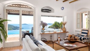 A spacious living room with a white sofa, a coffee table, and a view of the sea through large windows.