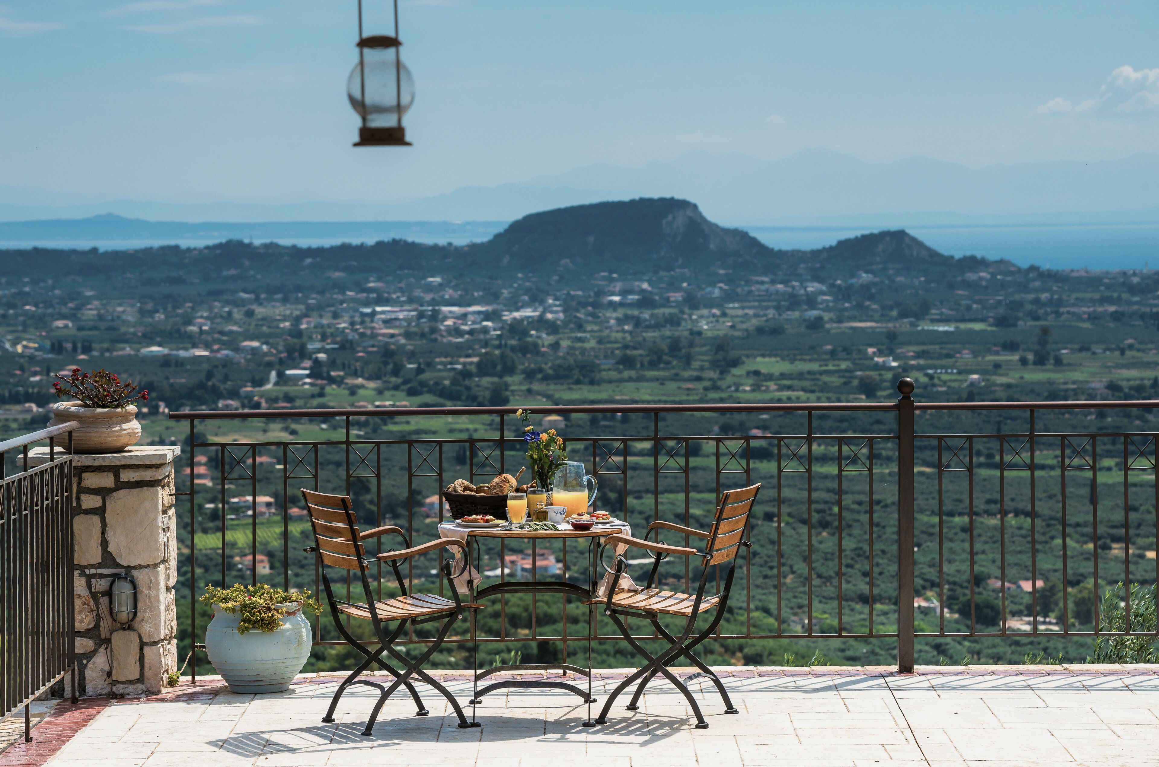 A balcony with a table set for two, overlooking a scenic landscape.