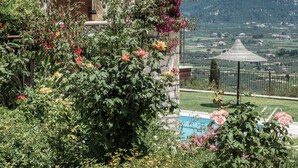 A stone building with a tiled roof, a wooden door, and a view of a pool and mountains in the background. - Agrikia One Bedroom Apartment (Zakynthos)