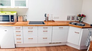 Een kleine keuken met witte kastjes, een magnetron, een spoelbak en een kleine koelkast.