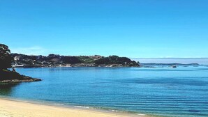 Eine Küstenlandschaft mit klarem, blauem Wasser, einem Sandstrand und einer fernen Uferlinie mit Gebäuden.