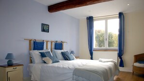 Quarto com uma cama grande, cabeceira de madeira, mesa de cabeceira com abajur, uma cadeira e uma janela com cortinas.