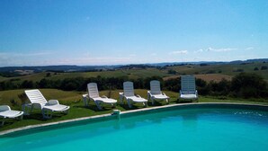 Piscina com cadeiras de descanso brancas e vista para colinas ondulantes.