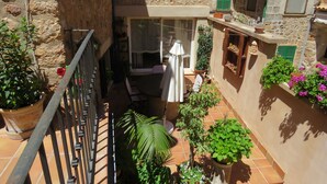 Un patio estrecho con balcón, plantas en macetas y un pequeño espacio para sentarse.