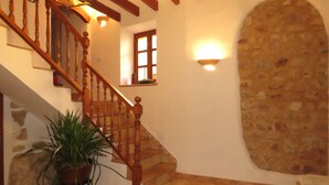 Una escalera con balaustres de madera, una planta en maceta y un muro de piedra.