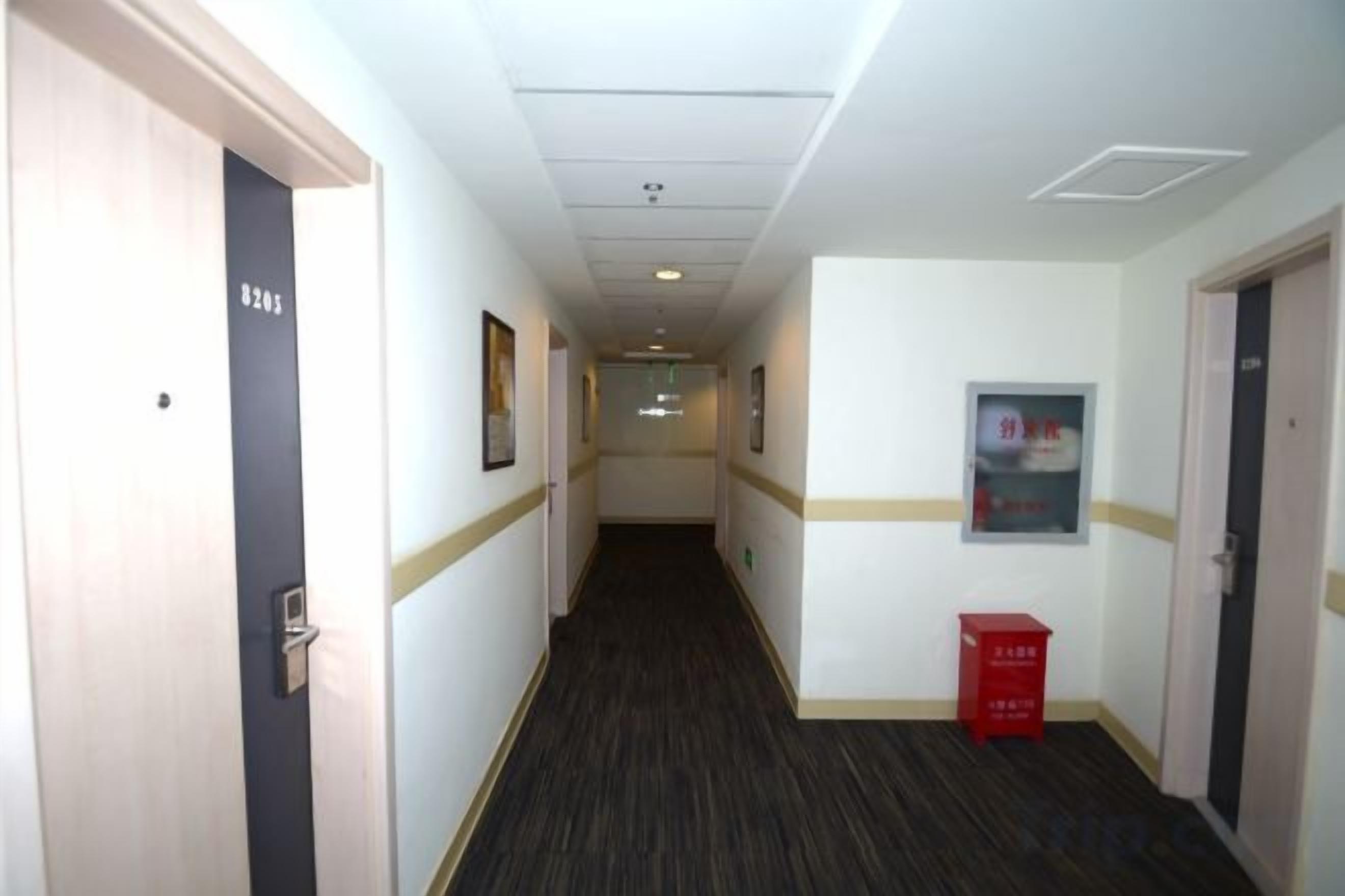 A hotel corridor with doors, framed pictures, and a red box on the floor.