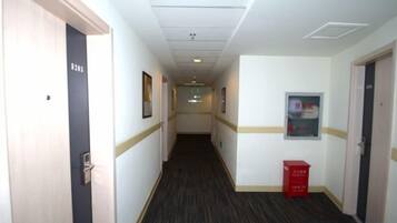 A hotel corridor with doors, framed pictures, and a red box on the floor.