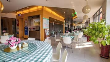 A hotel dining area with round tables, chairs, and potted plants.