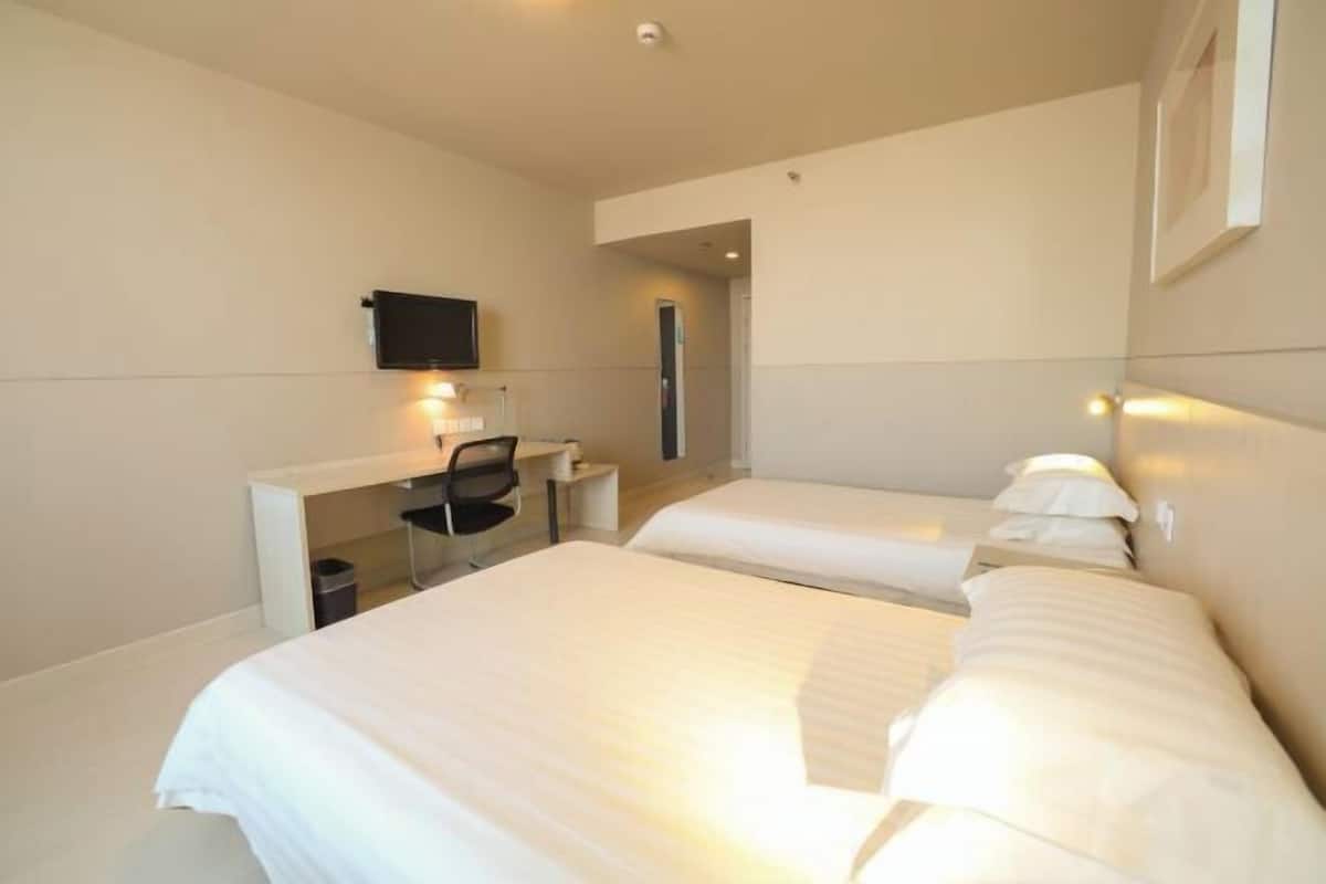 A hotel room with two beds, a desk with a chair, a television, and a small trash bin.